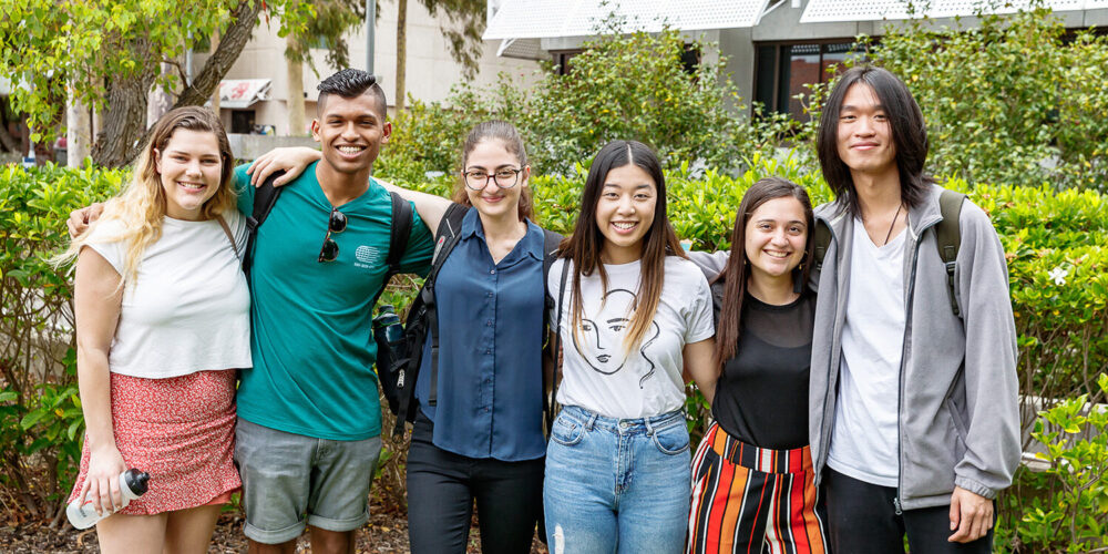 Group of 6 friends standing together with their arms around each other - play video