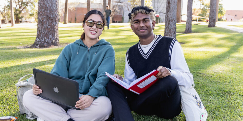 Two people sitting on grass together smiling at camera - play video