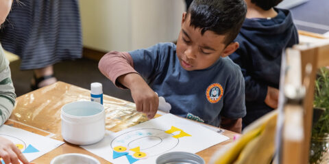 Child gluing paper onto a collage