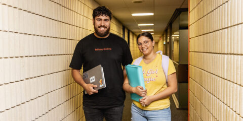 Two students standing in hallway smiling at camera