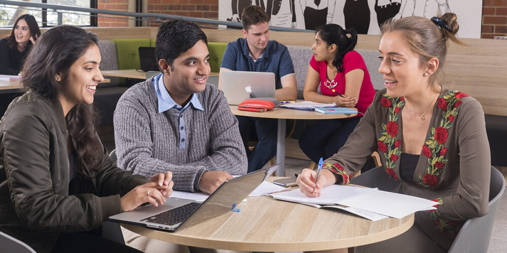 Three people in foreground talking around a small circular table, with other people in the background on their own circular background