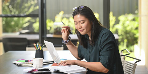 A student sitting on her dining table with her laptop and study tools in front of her