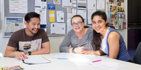 Three people sitting a desk with writing materials in front of them