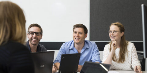 Group of people wearing business attire looking at someone, all with laptops open