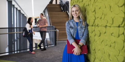 female student leaning against the wall and smiling