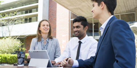 3 Office workers sitting outside discussing about something while looking at an ipad