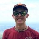 Photo of man in red shirt wearing glasses, with scenic background