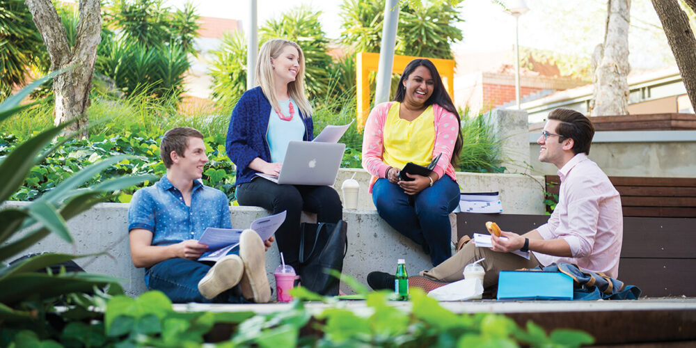 4 people talking with each other outside, with study materials - play video