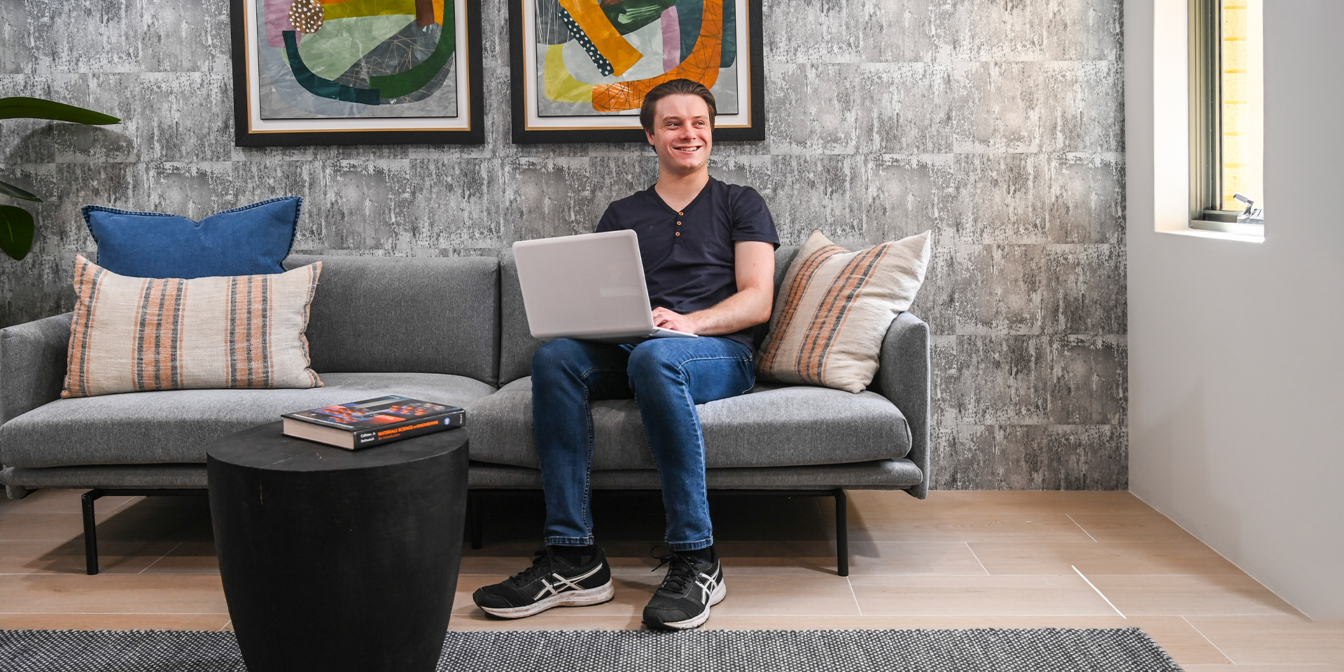 Male student sits on a sofa with a laptop in his hand