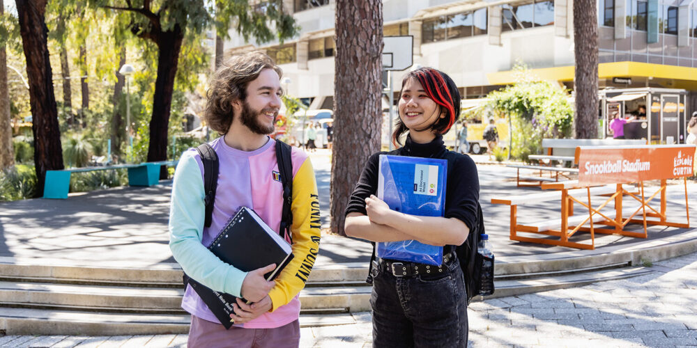 2 students smiling at each other while walking on a path