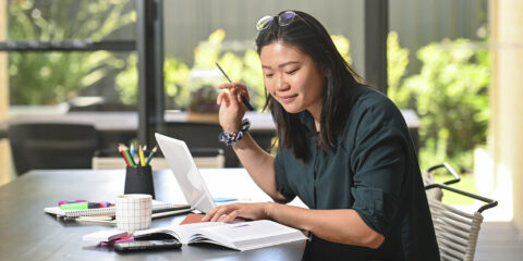 student reading her textbook with her laptop open beside her