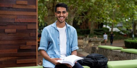 student sitting outside and smiling while reading a book