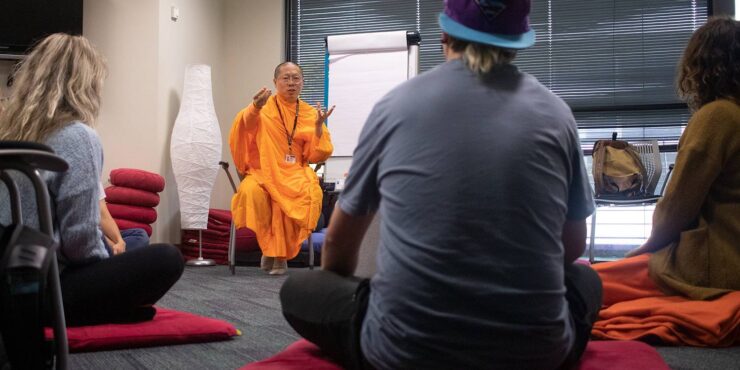 People listening to a Buddhist monk preach, while sitting on the ground